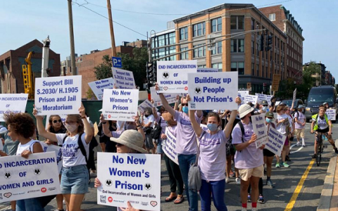 Protesters in street hold signs, No New Women's Prison