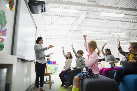 teacher pointing to students with hands raised - Instruction Partners