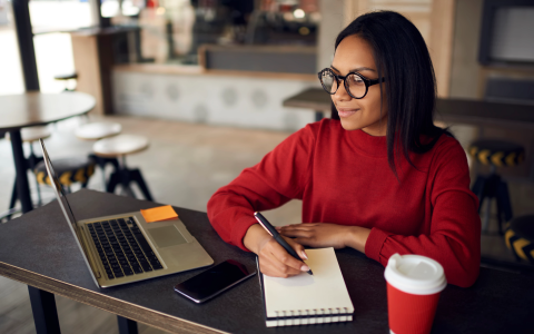 Reporter with pen, pad, laptop, phone, coffee on her desk